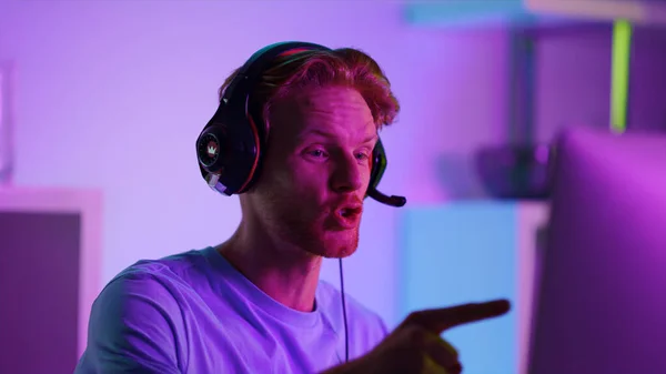 Excited man celebrating cyber tournament success closeup. Happy gamer in neon room playing computer video games on weekend night. Joyful ginger guy player enjoying triumph winning battle in cyberspace