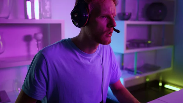 Esport professional playing home in neon lights closeup. Frustrated ginger man losing checking game results after arcade round. Focused gamer looking computer screen resting in cyberspace room weekend