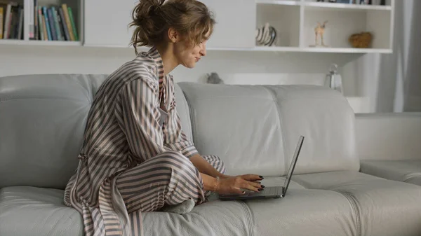 Freelancer working home workplace closeup. Girl drinking coffee in living room. Sleepy manager yawning stretching body resting on sofa morning. Attractive woman open laptop start working day remotely