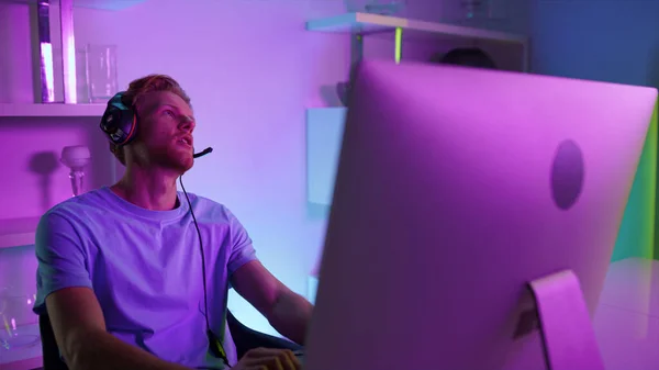 Upset gamer looking computer checking cyber competition results at home closeup. Disappointed man losing video game in neon lights room. Sad esport professional playing arcade in headset weekend night