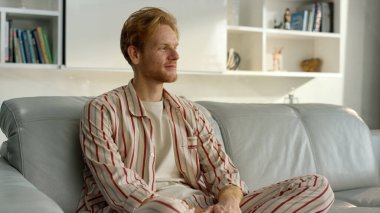 Mutlu adam sakin ev atmosferinin keyfini çıkar. Kanepede pijamalarıyla dinlenen serbest çalışan biri. Tatmin olmuş işadamı kızıl adam, taşındıktan sonra dinlenme odasında poz veriyor. Rahat bir evde sakin bir sabah.