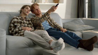 Evli çift birlikte dinleniyor. Kızıl saçlı koca televizyon kanalını araklıyor. Genç bir aile televizyon izleyip, iç mekanda dizi seçiyor. İki mutlu arkadaş film haftasonunda takılıyorlar..