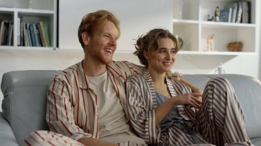 Evli insanlar pijamalarıyla kanepeye sarılıyorlar. Mutlu aile sabah tatilleri. Gülümseyen kızıl koca, çekici karısına yeni evini kucaklıyor. Neşeli çift konuşuyor. Hafta sonları huzurlu atmosferin tadını çıkarın..