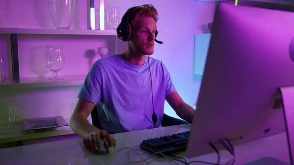 Man having live stream in neon room. Joyful gamer commenting actions in headset. Cyber game player enjoying shooter tournament communicating with team. Student resting hang out with friends remotely