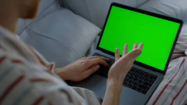 Man talking green laptop resting on sofa closeup. Teacher having online lecture at remote home office. Unrecognized freelancer waving greeting client friend lying in pajamas. Mockup computer concept.