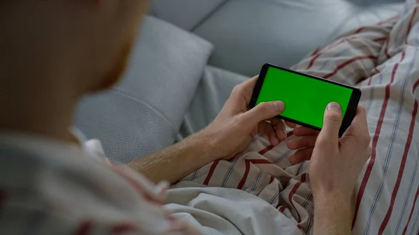 自宅のスマートフォンに緑の画面を入力する男 プレイヤーはオンラインゲームの閉鎖をお楽しみください 認識されていない人は クロマキー携帯電話でスマートフォンのテキストブラウジングインターネットを保持します モックアップ電話を使った無名の男 — ストック写真