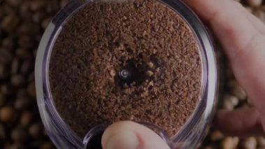 Elektrikli öğütücüde dönen öğütücü kahve üst görüntüyü kapatır. Bilinmeyen barista el ele tutuşup modern değirmende içki için aromatik malzemeler hazırlıyor. Mutfak ekipmanları içeride kahve taneleri öğütüyor.
