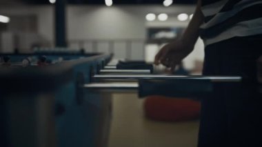 Enerjik çocuk elleri yakın çekimde masa futbolu oynuyor. Tanınmayan aktif okul çocuğu gol atmaya çalışırken oyun yarışmasından zevk alıyor. Boş okul lobisinde langırt sopası çeken neşeli genç adam.. 
