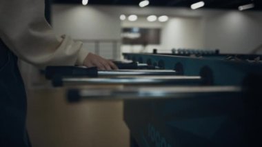 Kız elleri masa futbolu çubuklarını kavrıyor. Bilinmeyen enerjik liseli kız boş kampüs salonundaki derslerden sonra langırt maçının keyfini çıkarıyor. Modern okul lobisinde aktif genç öğrenci oyunu oynuyor..
