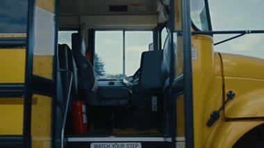 Okul otobüsü girişi boş durakta öğrenci şoförü kapatmadan açılır. Cam kapılı çocukların akademik taşınma gününün güneşli görüntüsü. Güvenli sarı araç öğrencileri dersten sonra evlerine giderken bekliyor..