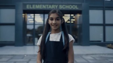 Sınıflar kapandıktan sonra tek başına modern kampüs girişinde duran gülümseyen Hintli kız. İlkokul bahçesinde sırt çantası takan neşeli, sevimli bir genç. Kamu eğitimi kavramı.