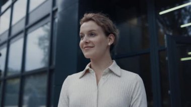 Gülümseyen kadın öğretmen yakından bak. Modern cam eğitim binasında tek başına poz veren genç bir okul çalışanı. Çekici sarışın akademisyen kampüste çocukları karşılıyor.. 