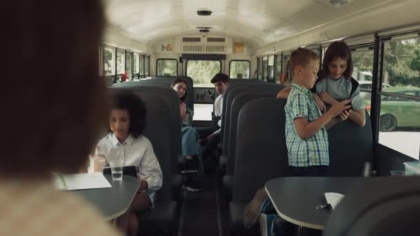 不同的学生坐在校车上等待旅行 一群多民族的孩子在学校的校车里玩游戏 快乐的小学生在回家的路上使用现代小玩意 学习概念 — 图库视频影像