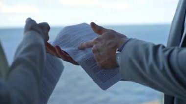 Deniz manzarasında kontrat detaylarını gösteren bir adam. El ele tutuşup belgeyi yakınlaştırın. Tanınmayan işletme yöneticileri proje anlaşmasını inceliyor. Patron profesyonel pazarlama raporunu kontrol ediyor.