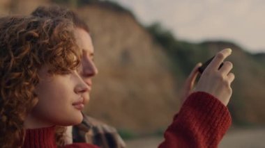 Gündoğumu plajında akıllı telefondan fotoğraf çeken rahat aşıkların portresi. Yan görüş odaklı çift yüzleri günbatımının tadını çıkarıyor. Deniz kıyısında duran hayalperest arkadaşlar. Günlük için cep telefonu kullanan kız