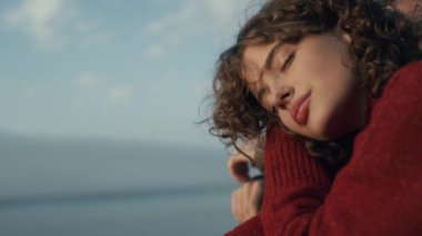 Deniz sahilinde oturan göz kamaştırıcı kız. Romantik bir kadın okyanusta vakit geçirmekten zevk alıyor. Kadın model, kıvırcık saçlara elleriyle dokunuyor. Gözleri kapalı rüya gibi bir kadının portresi. Yaşam tarzı kavramı