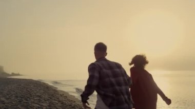 Güneşin doğuşunda kumlu sahilde koşan çift. Deniz kıyısında dans eden pozitif kız ve erkek. Arkadaşların mutlu. Okyanusta yaz tatilinin tadını çıkaran oyuncu kadın ve erkek. Mutluluk kavramı