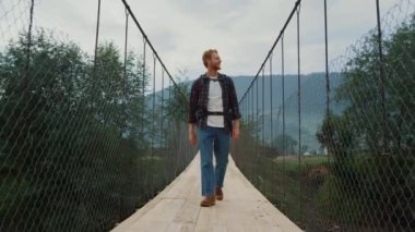 Gezgin adam kırsal dağlardaki köprüde yürüyor. Gülümseyen adam doğayı keşfeder. Aktif yürüyüş sporunda pozitif turistler sırt çantası giyer. Genç hippi haftasonunu dışarıda geçiriyor. Seyahat gezisi konsepti.