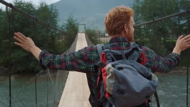 Рэкетир Прогуливается Мосту Через Горную Реку Рыжий Турист Наслаждается Походами — стоковое видео