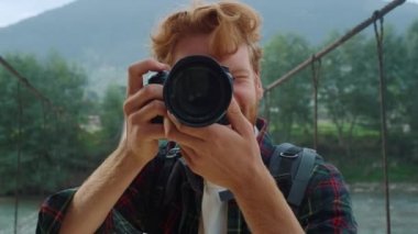Yürüyüşçü, profesyonel kamera merceğiyle fotoğraf çekiyor. Gülümseyen fotoğrafçı objektif bir şekilde yaz haftasonu dağ manzarası çeker. Seyahat blogunda hatıralar edinen mutlu bir turist. Hobi konsepti.