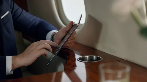 Closeup passenger holding tablet in hands. Stylish businessman touching screen browsing internet on corporate trip. Unrecognized successful investor ceo using digital pad checking sales statistics.