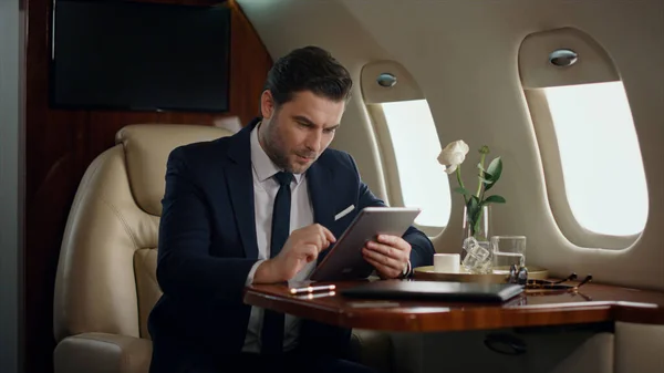 Stressed businessman working tablet in airplane. Professional touch pad screen checking company reports. Serious stylish ceo browsing web on business trip. Thinking man using digital computer in jet