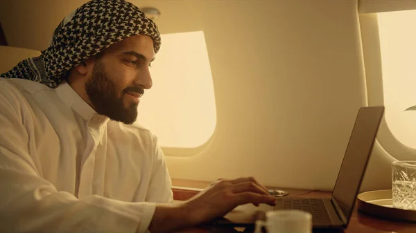 Confident leader browsing laptop on trip closeup. Focused arabian businessman using touchpad working on corporate trip. Successful company owner enjoy luxury flight surfing internet in muslim outfit.