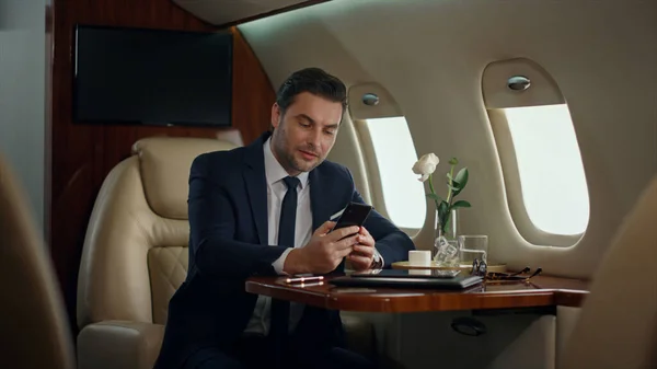 Busy man finishing phone call in luxury jet. Focused manager drinking coffee traveling business class airplane. Handsome businessman ending mobile conversation. Successful finance analyst talking cell