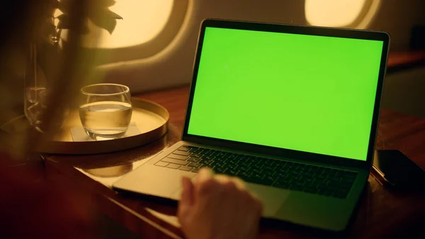 Woman watch green laptop screen on first class flight. Hands touch pad closeup. Unrecognized airplane passenger resting enjoy streaming platform show online. Manager working mockup computer on trip.