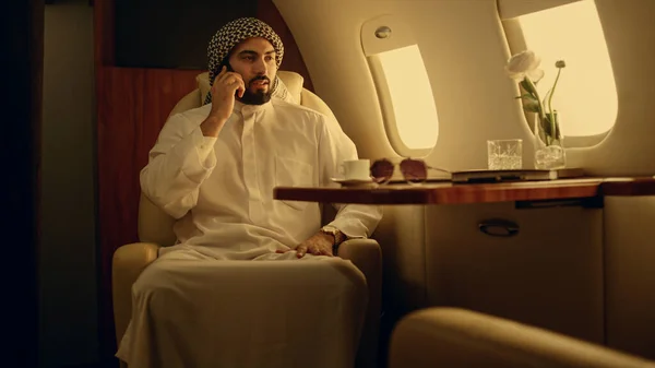 Professional speaking mobile phone in private jet. Businessman discussing work company deal in muslim clothing. Successful arabian company owner talk cell in luxury first class. Business trip concept
