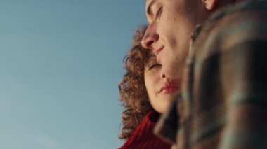 Loving couple posing at camera at low angle view. Smiling woman and man cuddling together outdoors. Closeup girl and guy touching faces. Lovers expressing tenderness to each other. Feelings concept 