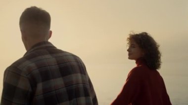 Loving couple dating on beach at sunrise. Happy woman and man walking on seashore. Romantic lovers holding hands together at date. Smiling girl enjoying sunset at ocean with guy. Relationship concept 