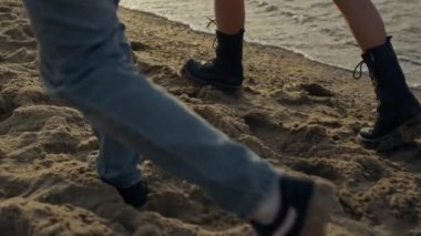 Closeup stylish woman and man feet walking on sandy beach. Romantic couple holding hands at sunset. Lovely girl and guy spending vacation at sea. Young family enjoying honeymoon. Travel concept 