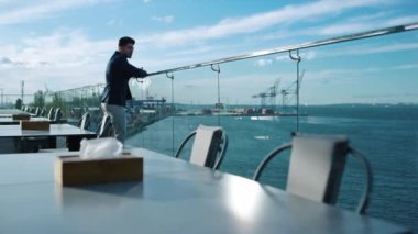 Businessman relaxing hotel terrace alone. Thinking man admire sea view morning. Successful manager investor waiting for client meeting on rooftop at commercial port cranes. Peaceful mood concept.