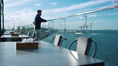 Pensive man resting alone on glass restaurant terrace. Freelancer looking sea port view in morning. Attractive businessman real estate manager waiting corporate client meeting. Guy thinking business
