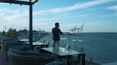Handsome man resting terrace at sea port view. Focused businessman thinking business problems enjoying calm morning in luxury cafe. Attractive brunette manager looking ocean relaxing on balcony alone