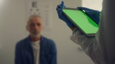 Muayeneden sonra doktor elleri yeşil ekran tablet cihazını kapatıyor. Modern hastane ofisinde kıdemli hasta terapisti ziyaret ediyor. Sağlık kliniğinde çalışan bilinmeyen bir doktor..