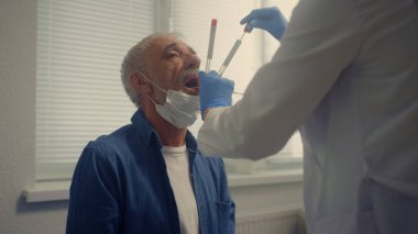 Sağlık kliniğinde tükürük testi yapan yaşlı bir hasta. Kadın doktor tüplü pamuk çubuğu kullanarak örnek alıyor. Modern hastanede bilinmeyen bir doktor DNA analizi yapıyor..