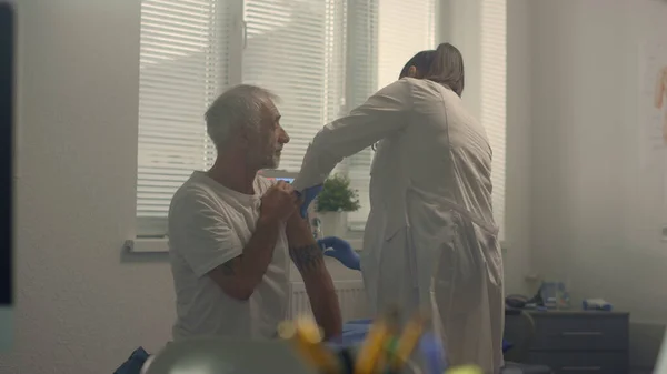 Physician vaccinate elderly patient in modern hospital office. Senior man getting vaccine injection in health clinic. Unknown woman doctor using syringe with antivirus preparation. Healthcare concept