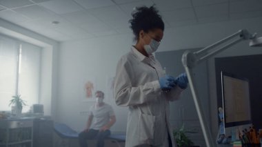 Aşıdan sonra omuz omuza tutulan hasta modern bir klinikte oturuyor. Maskeli kadın doktor tablet bilgisayardaki aşı verilerini daktilo ediyor. Afrikalı Amerikalı hekim iş yerinde teknoloji kullanıyor..