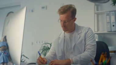 Modern çalışma masasında çalışan ciddi bir doktor. Adam doktor çevrimiçi danışmanlık için bilgisayar kullanıyor. Klinikte ilaç yazan genç bir terapist. Sağlık hizmetleri kavramı.