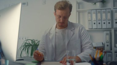 Modern klinikteki rahat doktor işyeri. Kapatın. Ciddi bir doktor hastasına kişisel bilgisayarını kullanarak danışmanlık yapıyor. Profesyonel terapist tıp dergisine not alıyor..