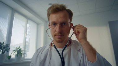 Dost canlısı doktor steteskop takıp modern klinik pov videosunda hastanın akciğerlerini kontrol ediyor. Genç bir doktor sağlık kliniğinde tıbbi malzeme kullanıyor. Sağlık hizmetleri kavramı.