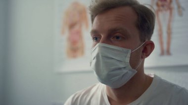 Portrait of tired patient waiting results quick coronavirus test wearing protective mask in hospital. Stressed young man sitting clinic office ready for vaccination close up. Healthcare in pandemic.