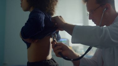 Orta yaşlı doktor akciğerlerini dinleyen genç kız tıbbi muayenede steteskop kullanıyor. Coronavirus 'tan sonra Afro-Amerikan çocuk doktoru muayenehanesine gitmiş. Salgın hastalıkta sağlık hizmeti covid19.