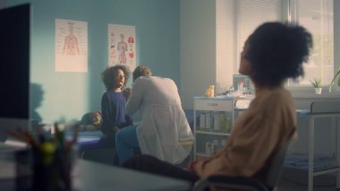 Çocuk doktoru Coronavirus belirtilerini kontrol etmek için kızın boğazını inceliyor. Afrikalı anne genel tıbbi konsültasyonu bekliyor. Bilinmeyen doktor açık çocuk ağzı arıyor. Sağlık hizmetleri kavramı.