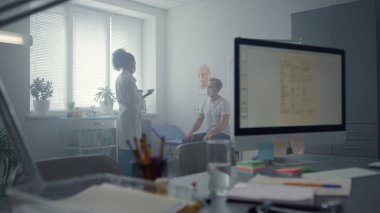 Çok ırklı kadın doktor, hastane ofisinde tablet bilgisayar uzmanı hasta kullanıyor. Ekranda veri sağlığı geçmişi olan teknolojik işyeri. Maskeli orta yaşlı adam hastalık belirtilerini anlatıyor..