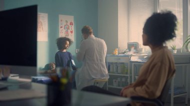 Annesinin yanında steteskoplu genç kız üzerindeki baskıyı ölçen kimliği belirsiz doktor. Afrikalı anne genel muayene için kızını getiriyor. Tıbbi danışma kavramı.