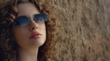 Portrait of sexy confident woman near sand hill outdoors. Closeup beautiful face young girl wearing stylish sunglasses. Serious seductive model posing looking camera on nature. Fashion glamour concept