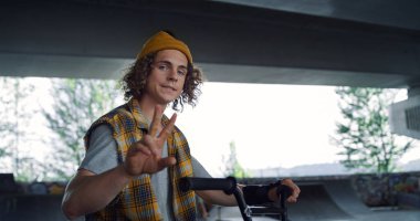 Paten parkındaki eğitimden sonra dinlenen şık bir adam. Dışarıda kamerada poz veren yakışıklı bir erkek. Paten parkında el kol hareketi yapan bir genç. Barış işareti gösteren olumlu bir adam. Kentsel alt kültür yaşam tarzı konsepti